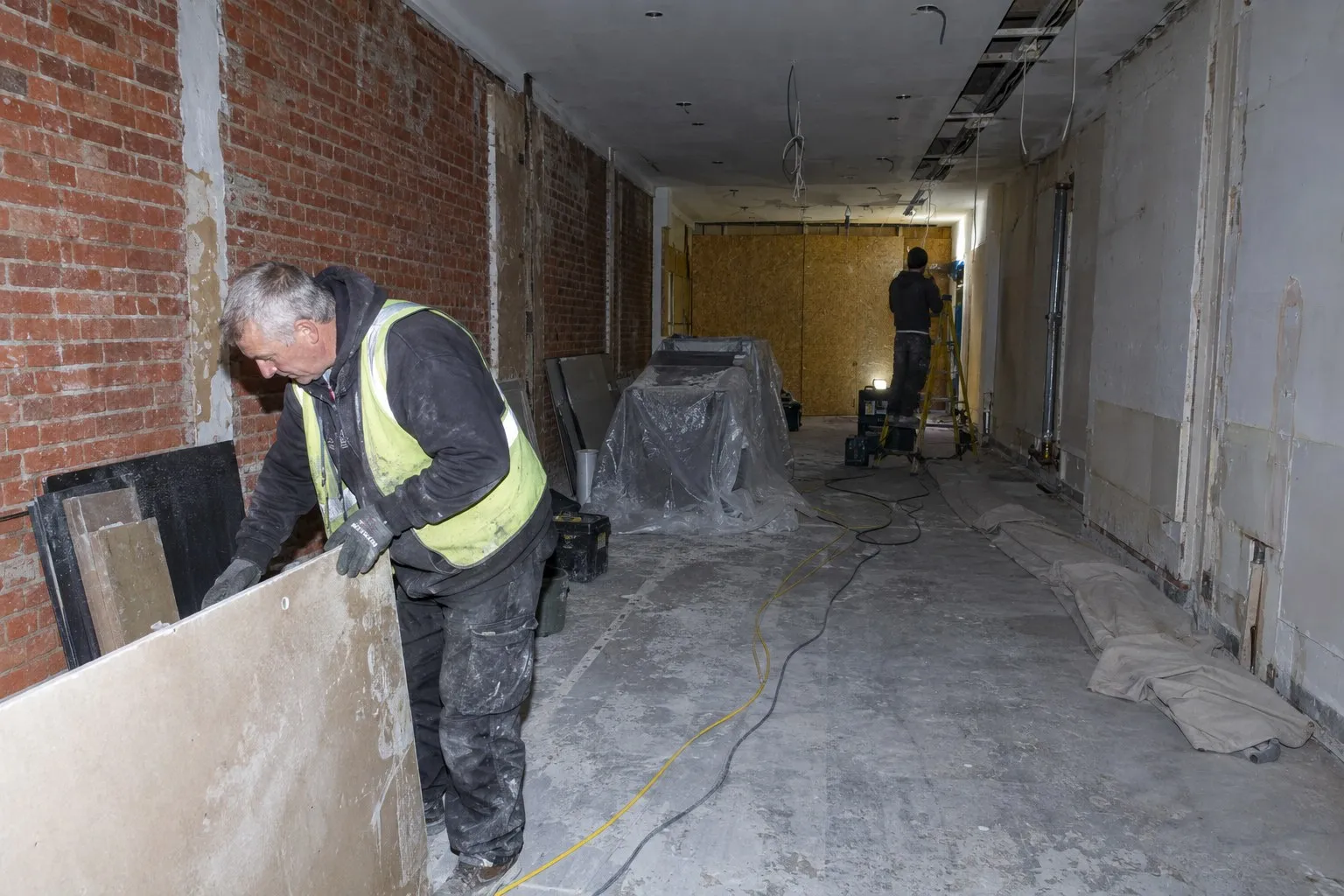 An empty high street shop floor stripped out for refurbishment, hoarding up and dust sheets down An empty high street shop floor stripped out for refurbishment, hoarding up and dust sheets down